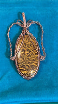 Copper wire wrapped Miriam stone pendant on teal background