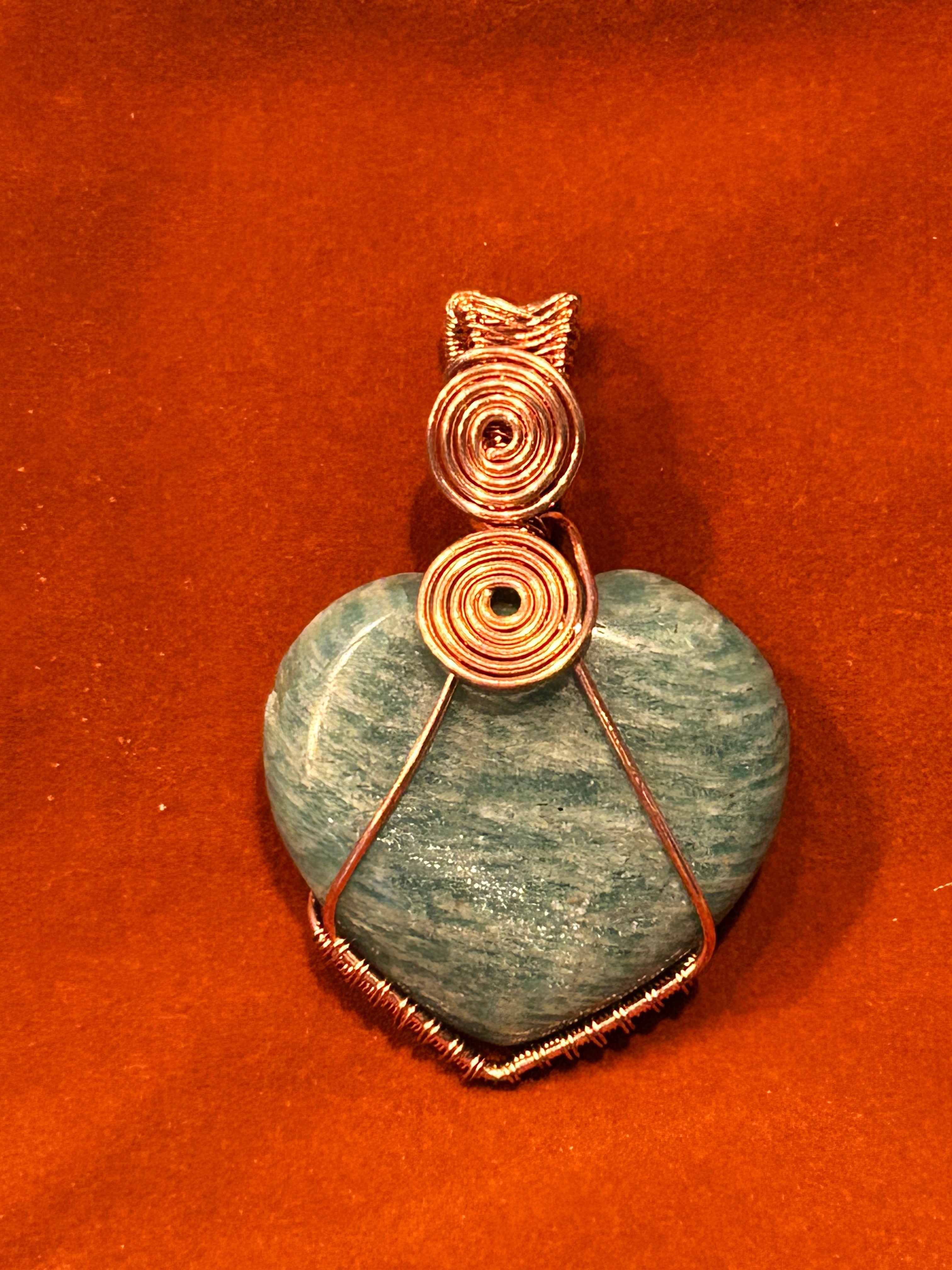 Copper wire wrapped teal Amazonite heart pendant with stacked double spiral bail on red-orange background