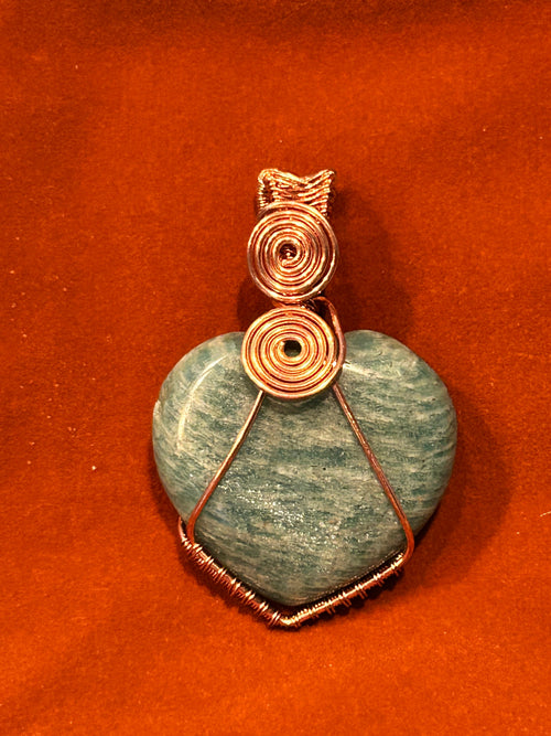 Copper wire wrapped teal Amazonite heart pendant with stacked double spiral bail on red-orange background