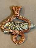 Copper wire sculpted snake pendant wrapped around brecciated jasper spike on tan background