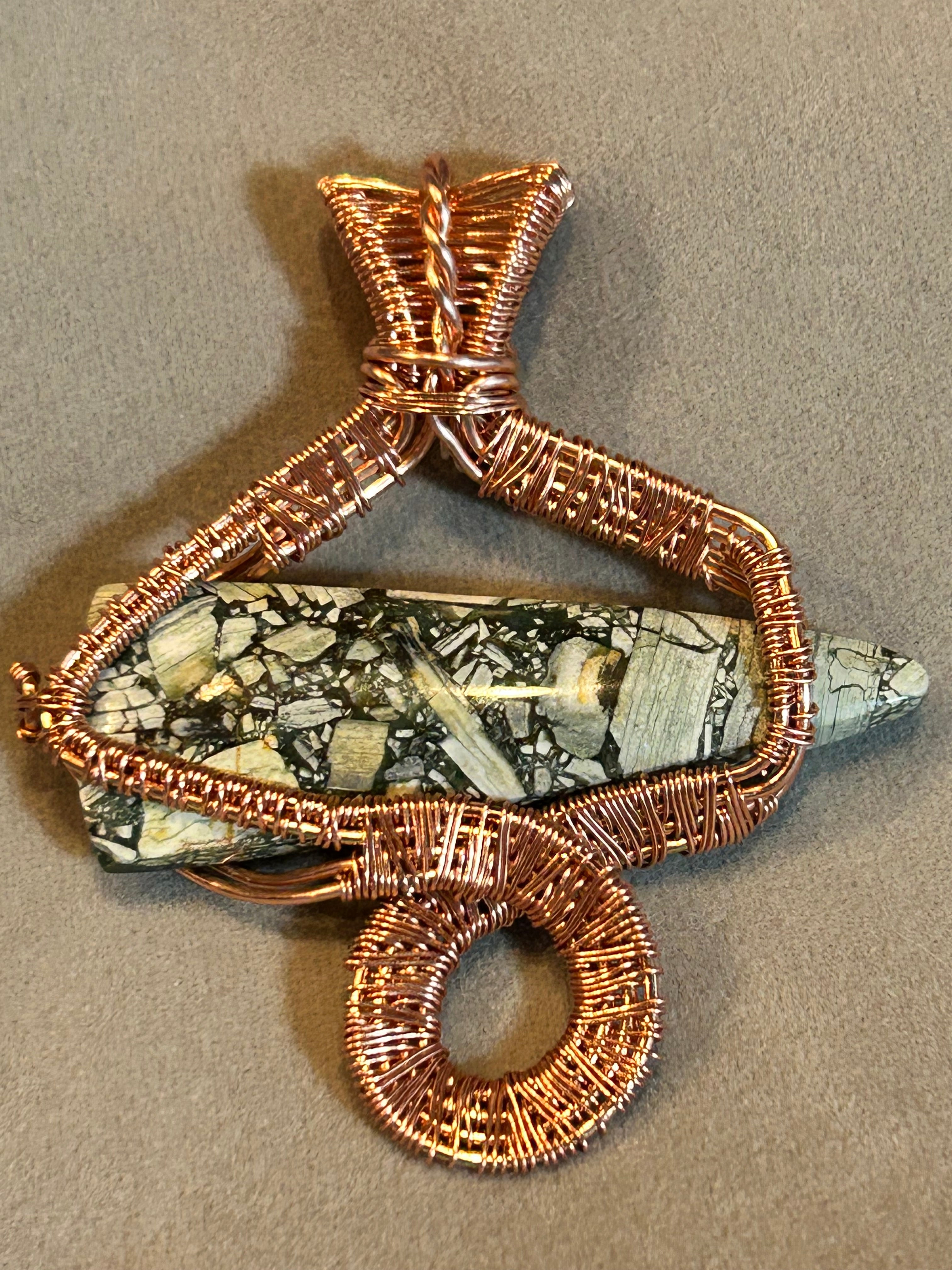 Copper wire sculpted snake pendant wrapped around brecciated jasper spike on tan background
