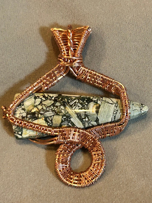 Copper wire sculpted snake pendant wrapped around brecciated jasper spike on tan background