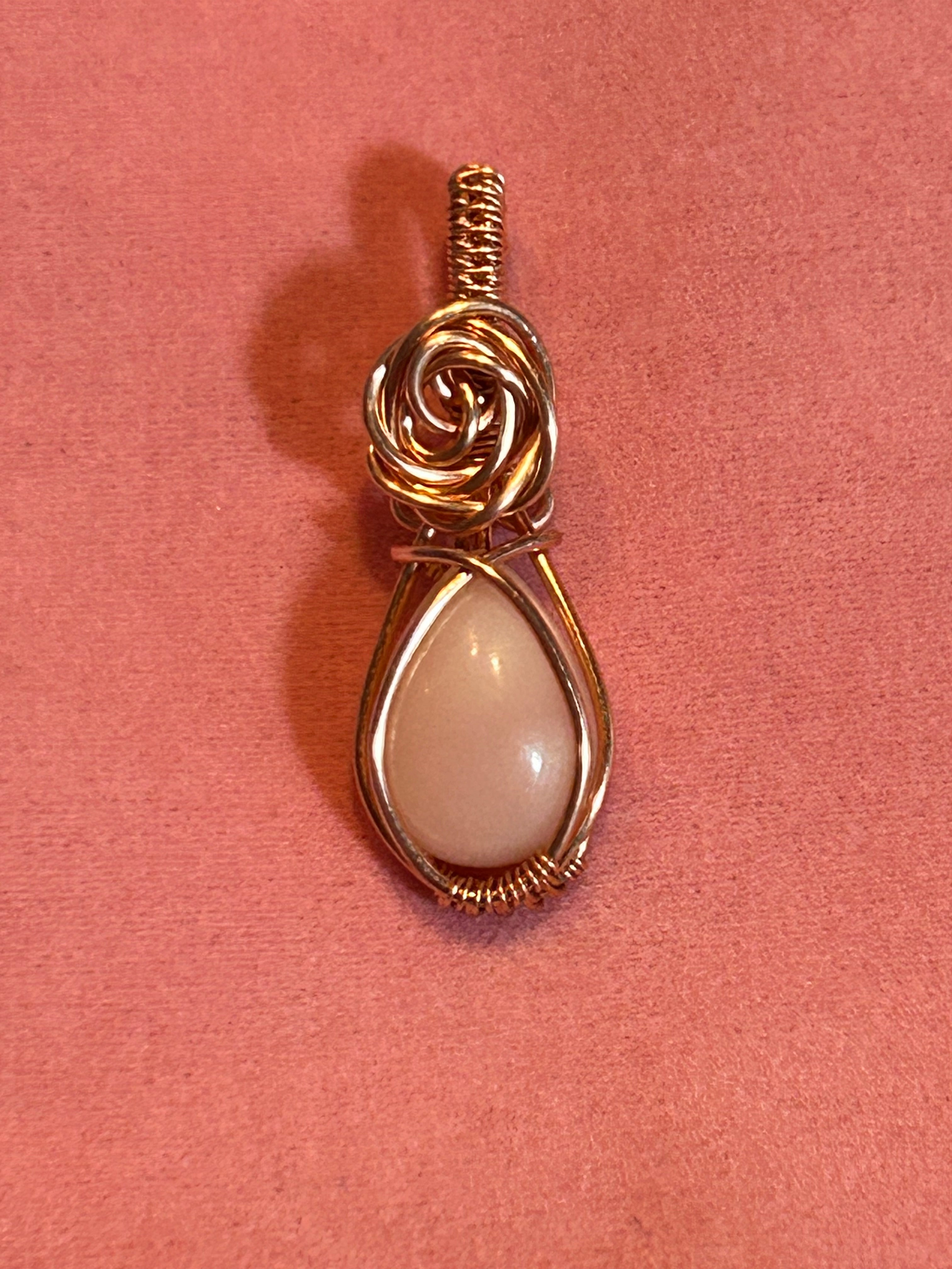 Copper wire wrapped pink opal teardrop pendant with hand-sculpted copper rose bail on pink background