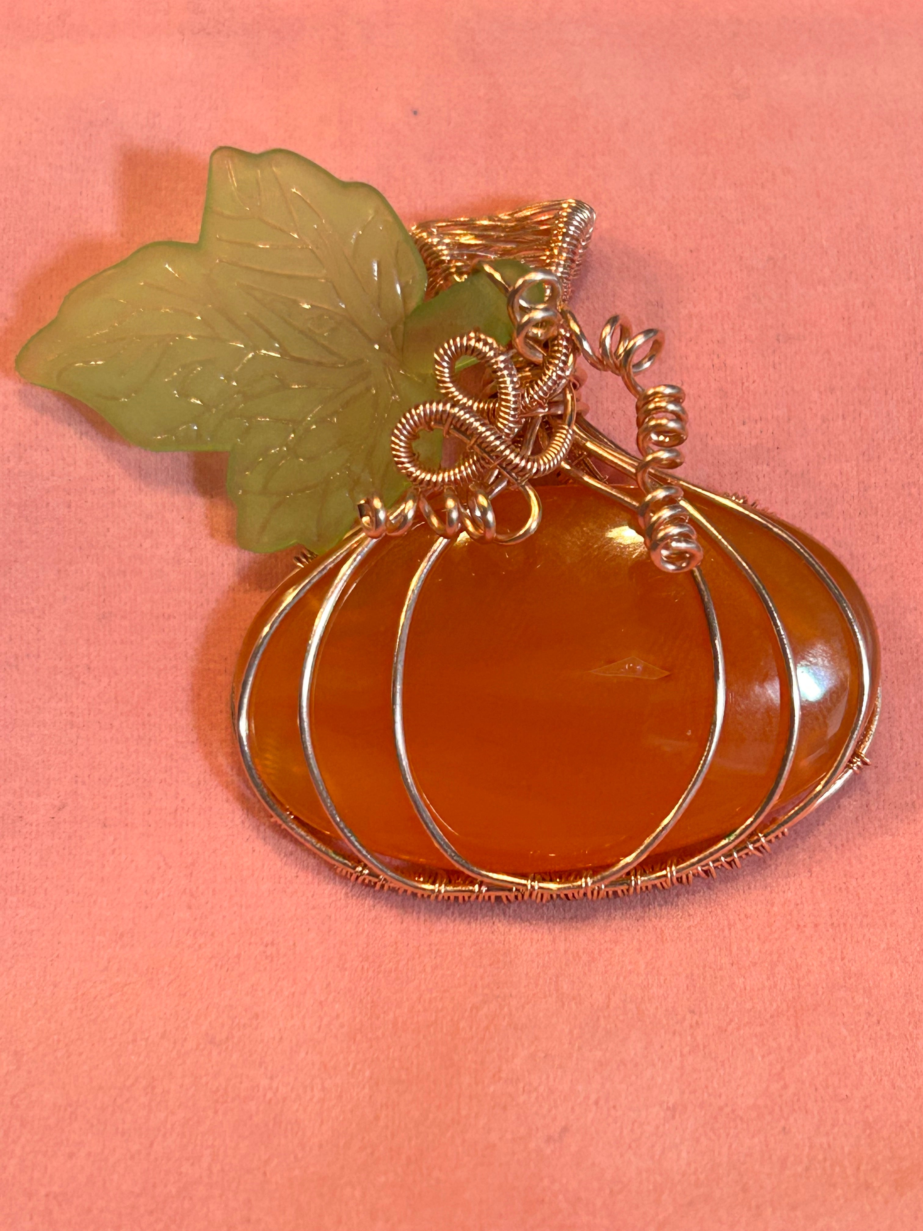 Copper and silver wire wrapped Carnelian pumpkin pendant with carved jade leaf and wire tendril on orange background