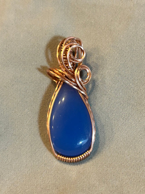 Copper wire wrapped cobalt blue onyx teardrop pendant with swirl bail on gray background