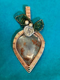 Copper and gold wire wrapped Aquaprase strawberry pendant with green wire leaves and silver rose on teal background