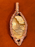 Copper braided wire wrapped Picture Jasper marquise pendant with crossed-wire base and silver bead bail on rust background