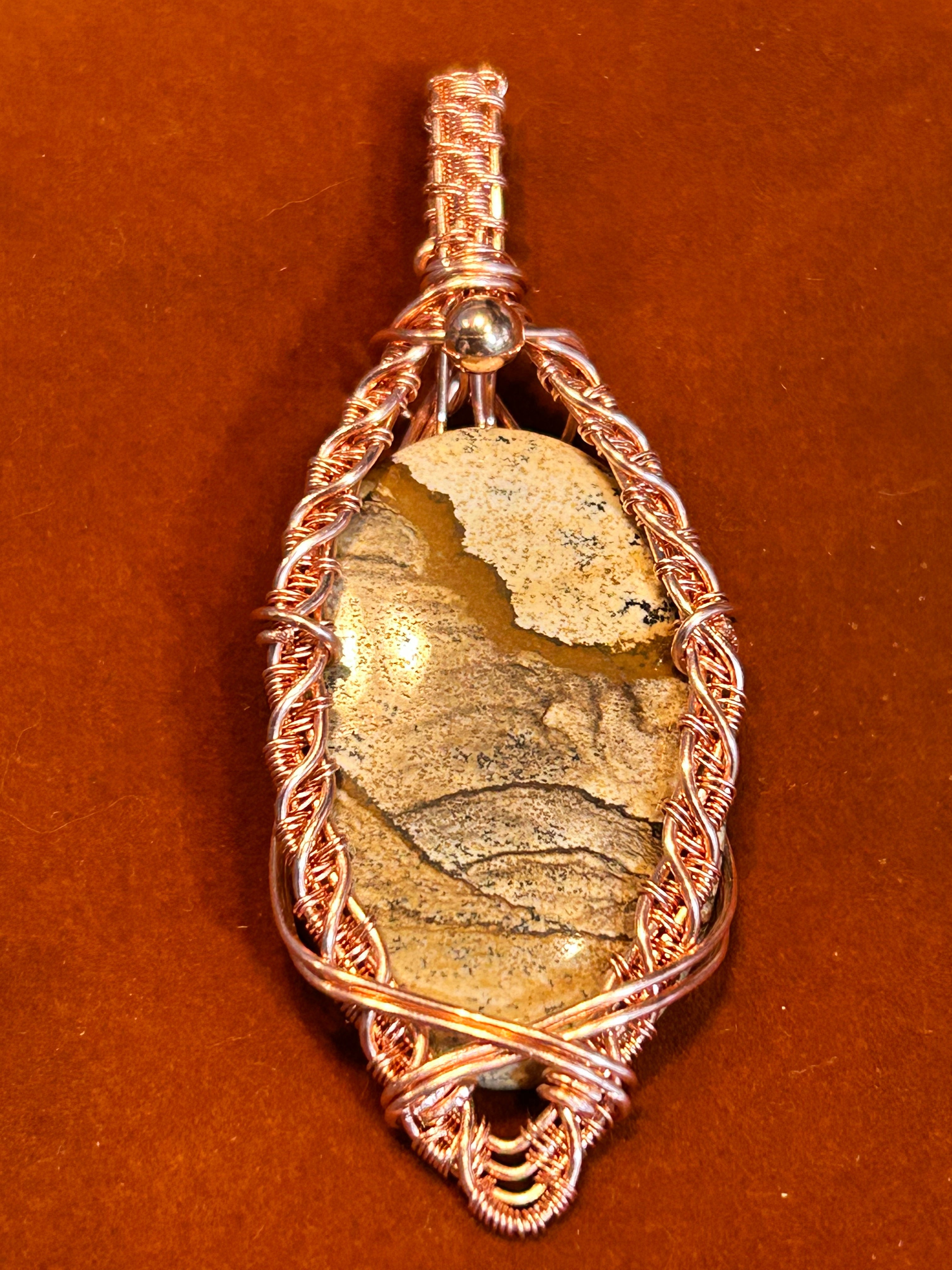 Copper braided wire wrapped Picture Jasper marquise pendant with crossed-wire base and silver bead bail on rust background