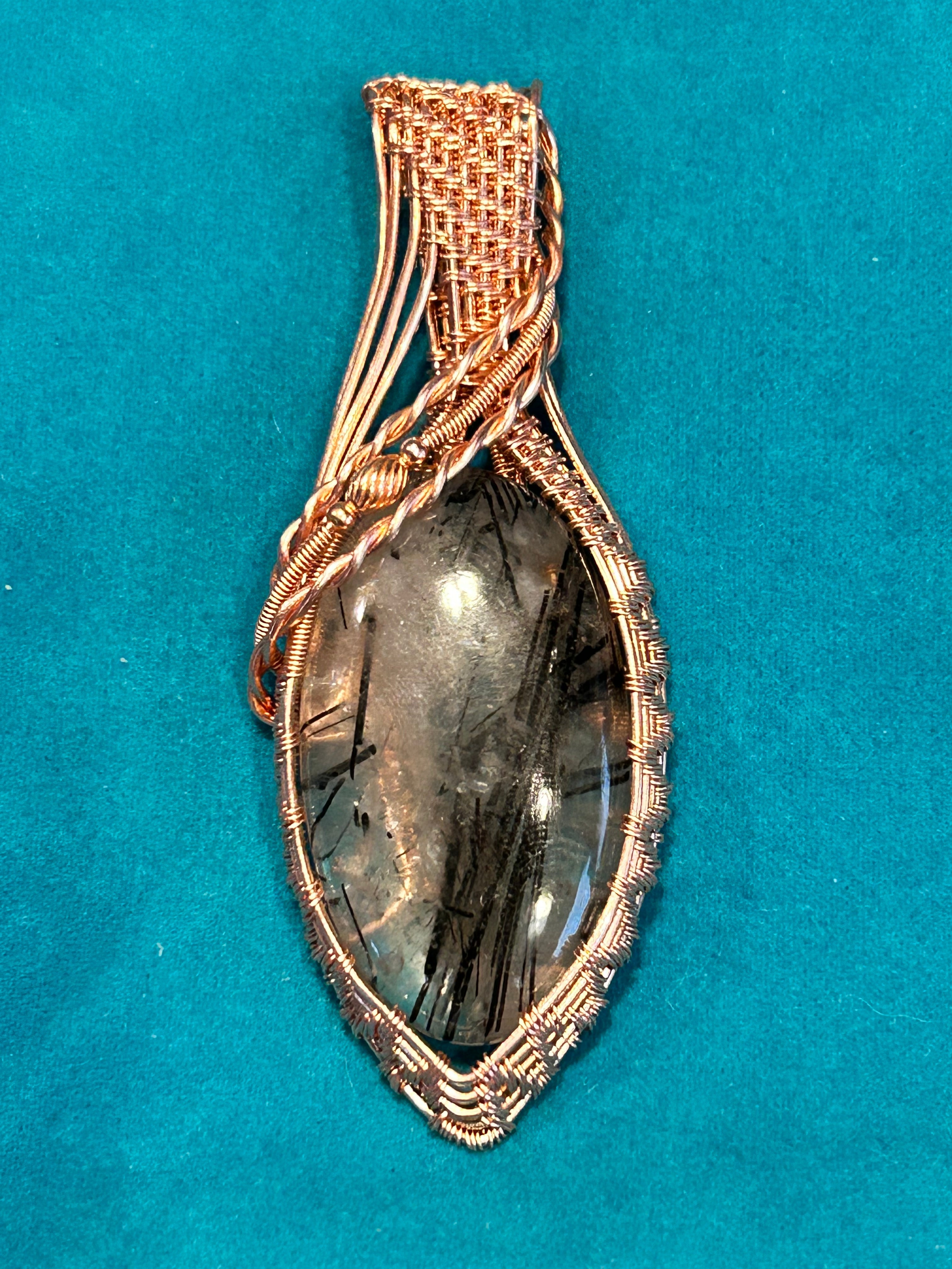 Copper basketweave wire wrapped Black Rutile Quartz marquise pendant on teal background
