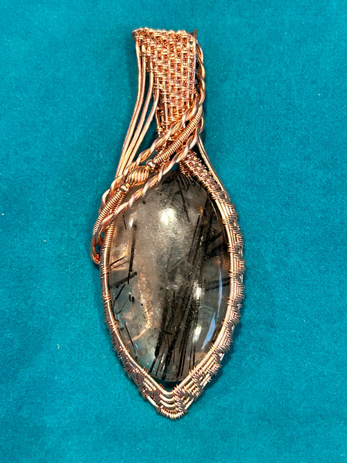 Copper basketweave wire wrapped Black Rutile Quartz marquise pendant on teal background