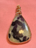 Copper basketweave wire wrapped Fluorite in Calcite triangular pendant with gold bead bail on pink background