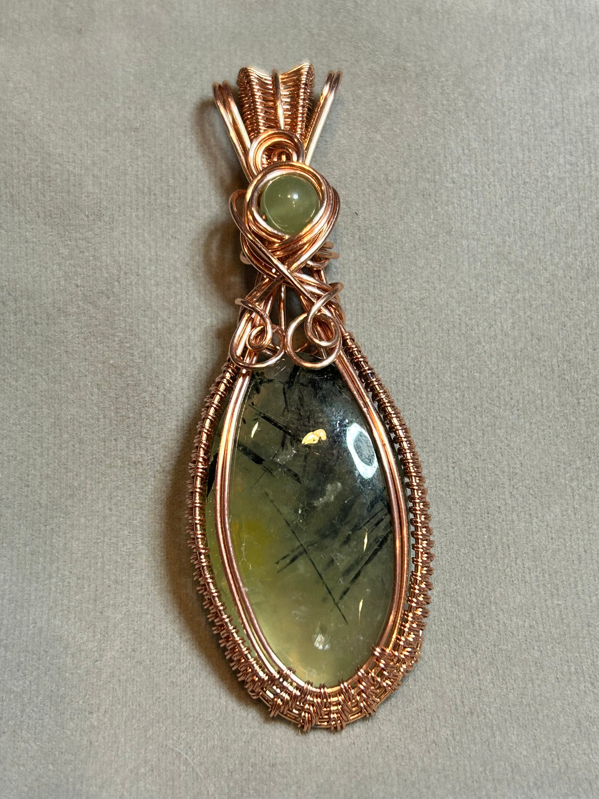 Copper basketweave wire wrapped Prehnite teardrop pendant with aventurine bead accent and scroll bail on tan background