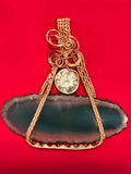 Gold wire wrapped deep teal dyed agate slice pendant with Swarovski crystal accent on red background