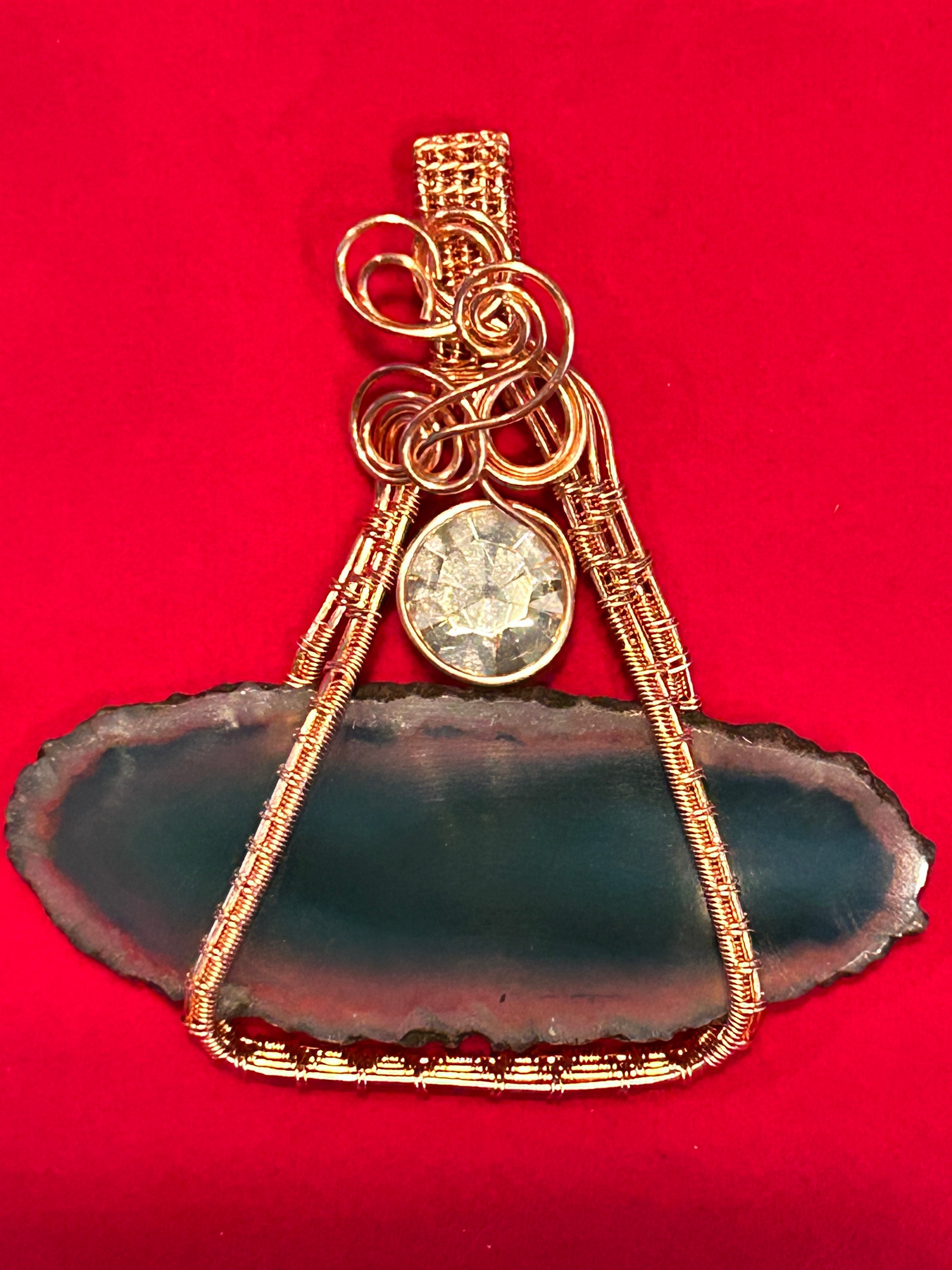 Gold wire wrapped deep teal dyed agate slice pendant with Swarovski crystal accent on red background