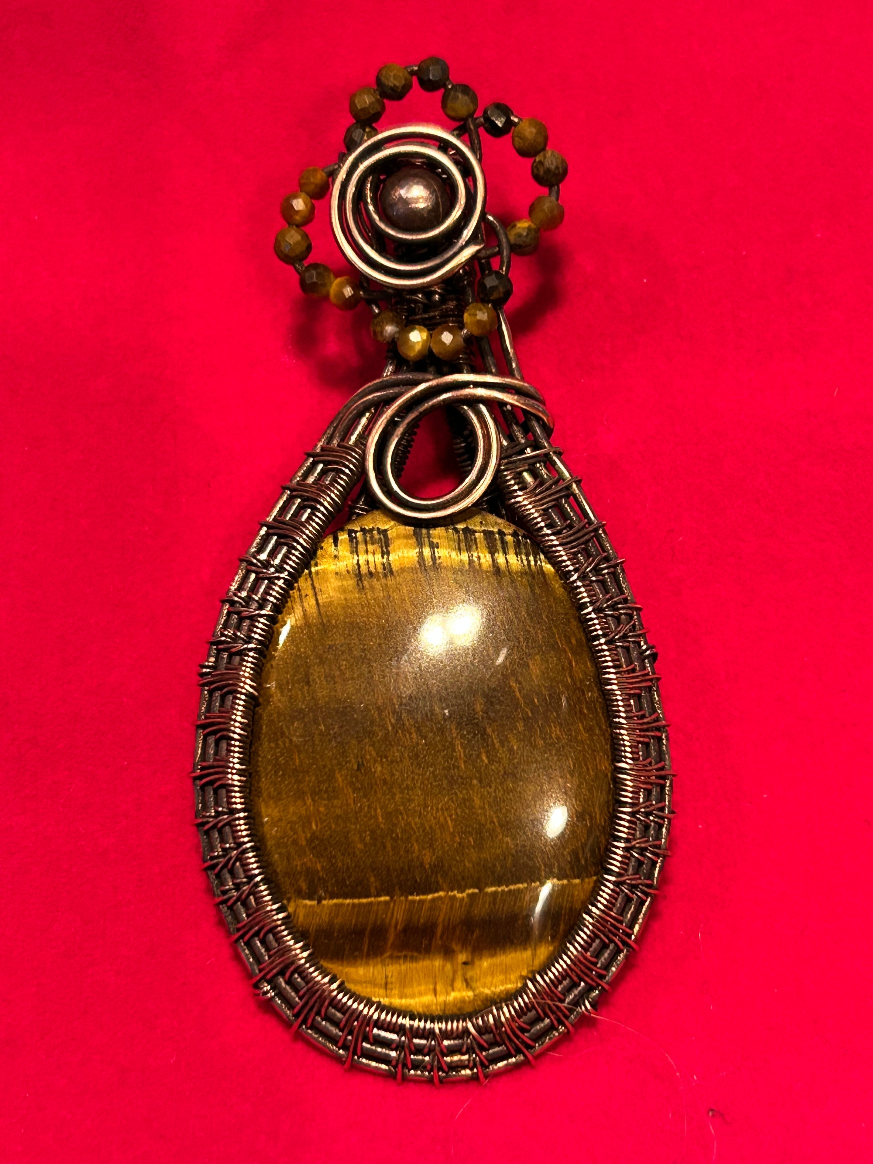 Copper basketweave wire wrapped Tiger's Eye pendant with Tiger's Eye bead bail accents on red background