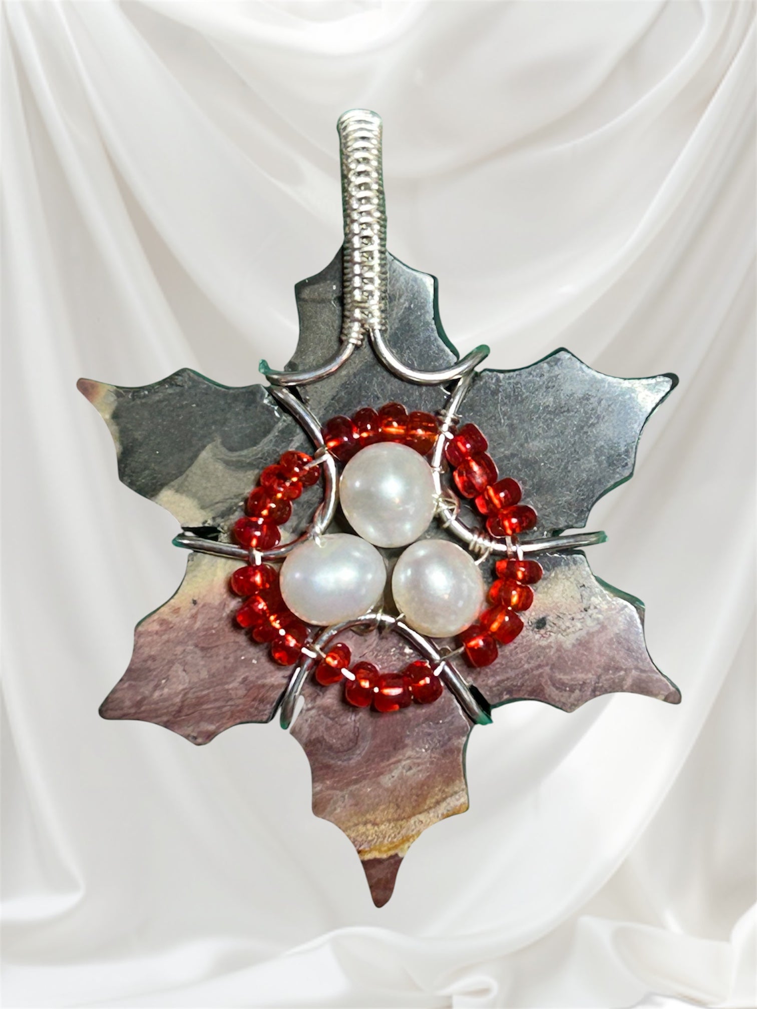 Silver wire wrapped petrified wood holly leaf pendant with freshwater pearl cluster and red seed bead ring on white background