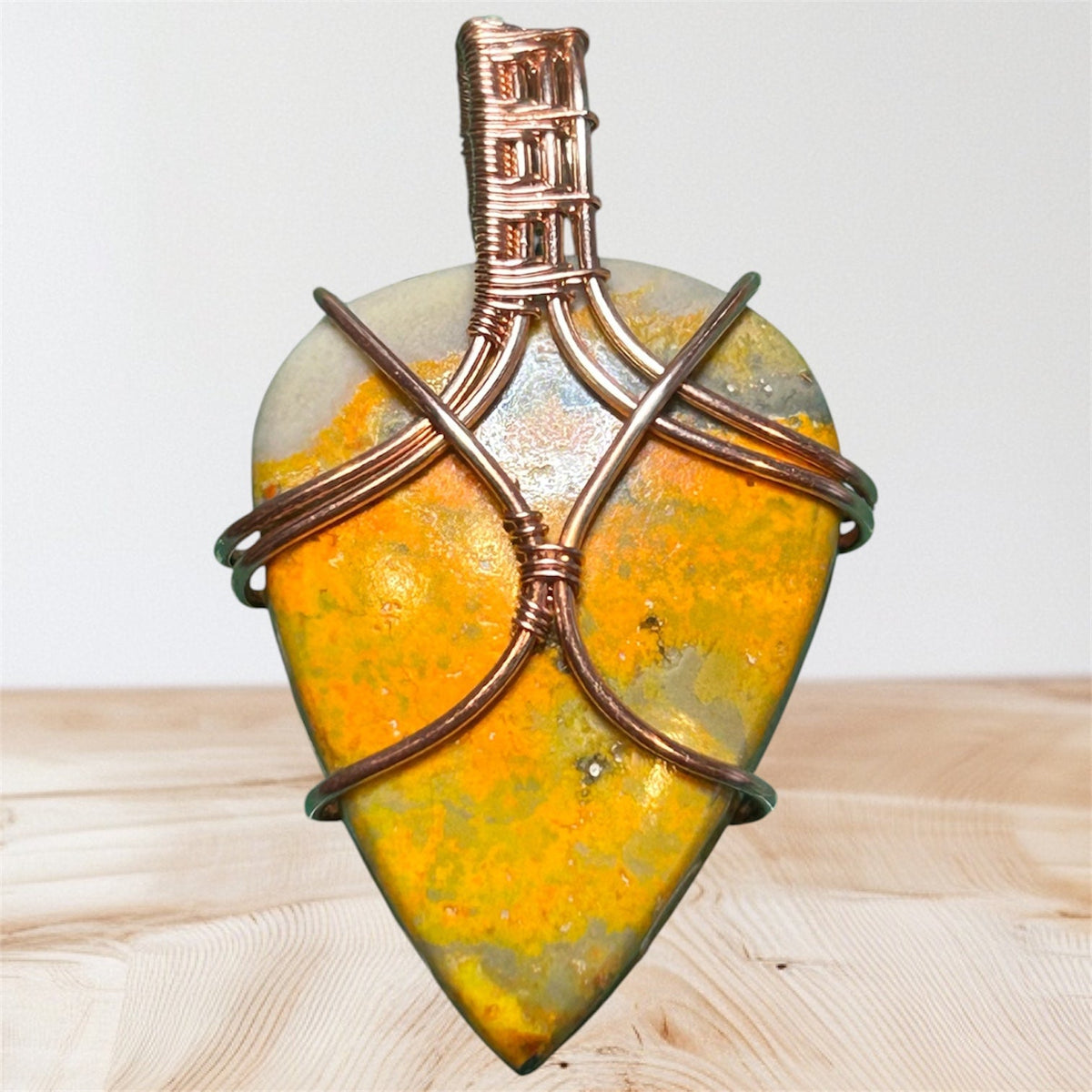 Copper wire wrapped Bumblebee Jasper guitar pick pendant with crossed wire detail and woven bail on wood background