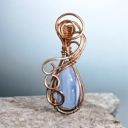 Copper wire wrapped blue opal teardrop pendant with sculptural swirl and loop bail on blue-gray background